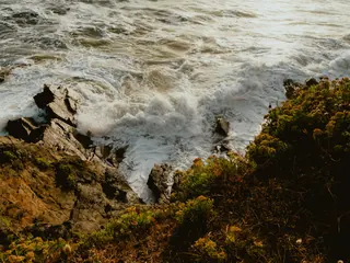 Une vague se brise sur des rochers bordés de végétation, sur la côte du Finistère.