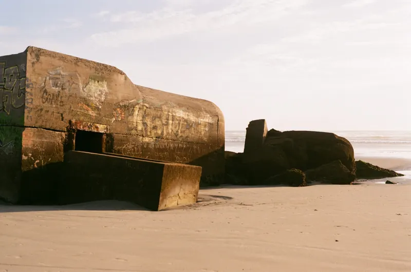 Deux blockhaus couverts de graffitis, à demi enfoncés dans le sable d’une plage, dans la lumière rasante du soir.