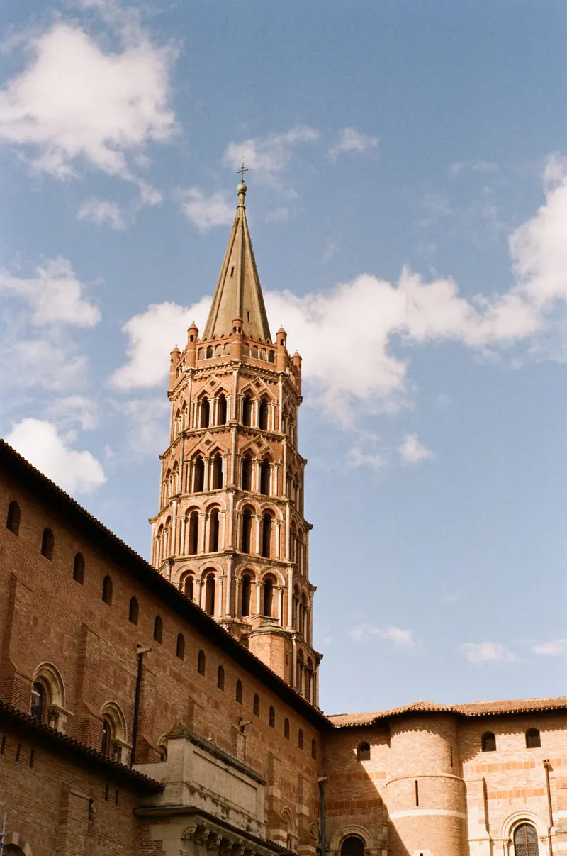 Le clocher octogonal en brique d’une basilique se détache sur un ciel bleu parsemé de nuages.