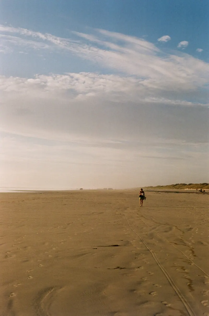 Une immense plage de sable au couchant, une silhouette isolée au loin, le ciel strié de nuages fins.