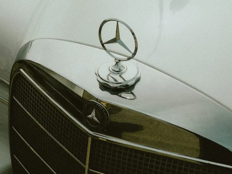 Gros plan sur l’étoile chromée et la calandre à grille d’une Mercedes ancienne, le capot clair renvoyant le reflet du ciel.