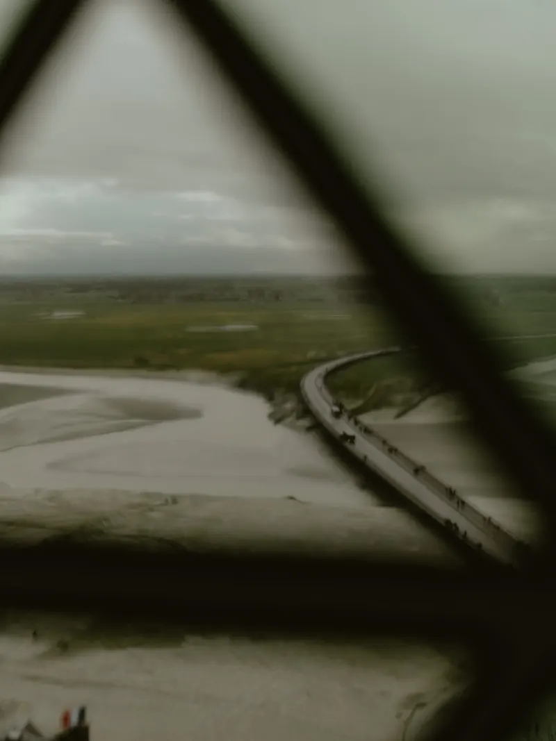 La baie et la passerelle vues d’en haut, à travers les montants flous et sombres d’une fenêtre.